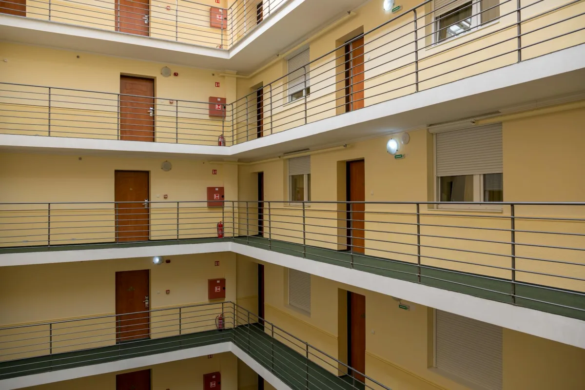 Un schéma en coupe d'un immeuble de quatre étages montrant les voies aériennes entre unités via les retours partagés, les gaines de plomberie et un ventilateur de pressurisation de corridor.