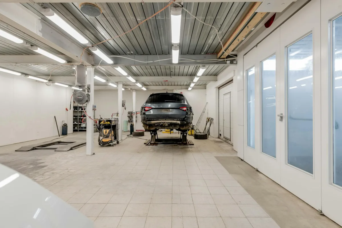 Une voiture stationnée dans un garage attenant, porte conducteur ouverte, légère vapeur d'échappement au pot.