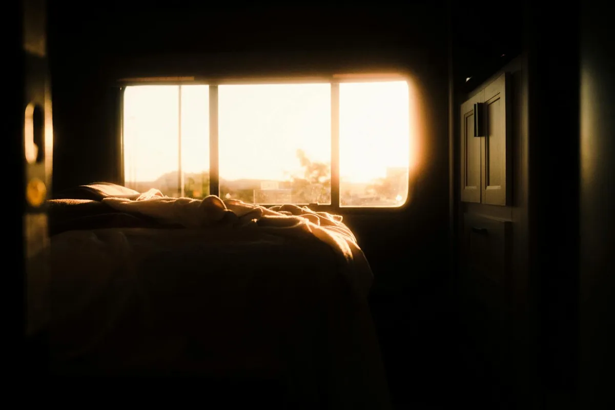 Une chambre à l'aube, draps froissés, fenêtre fermée, un mince trait de lumière à travers les rideaux.