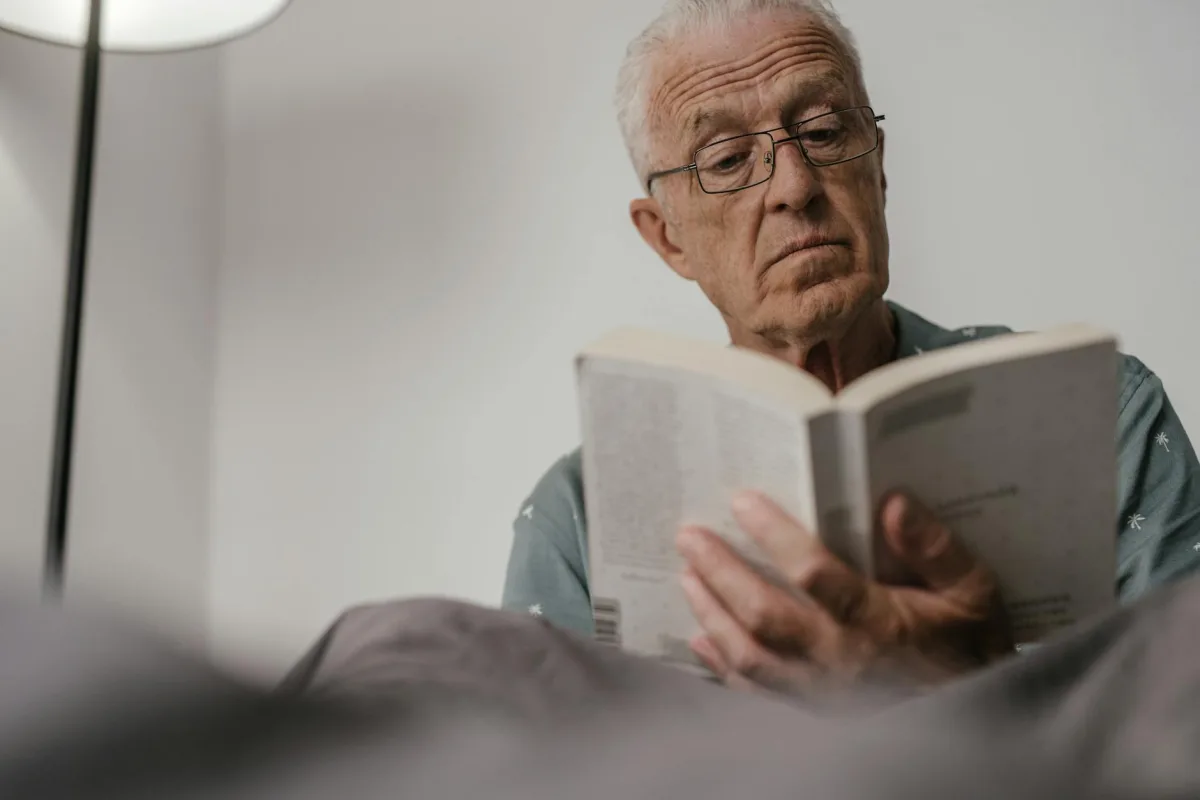 An older adult reading in a bright, plant-filled living room.
