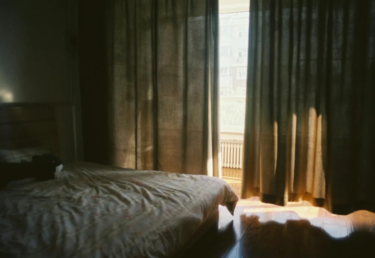 A bed with white linen in soft early-morning light, blinds half open.